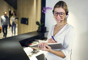 Smiling receptionist talking with headset while taking notes
